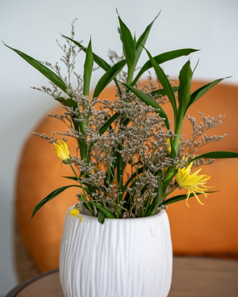 Yellow and green floral arrangement in a white vase on a wooden table with orange seating in the background at SOHO Sports Club Phuket.